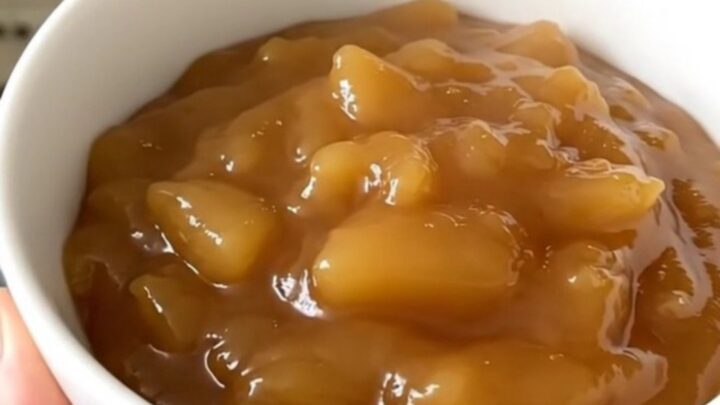 A white bowl filled with glossy, warm, and freshly made cinnamon applesauce.