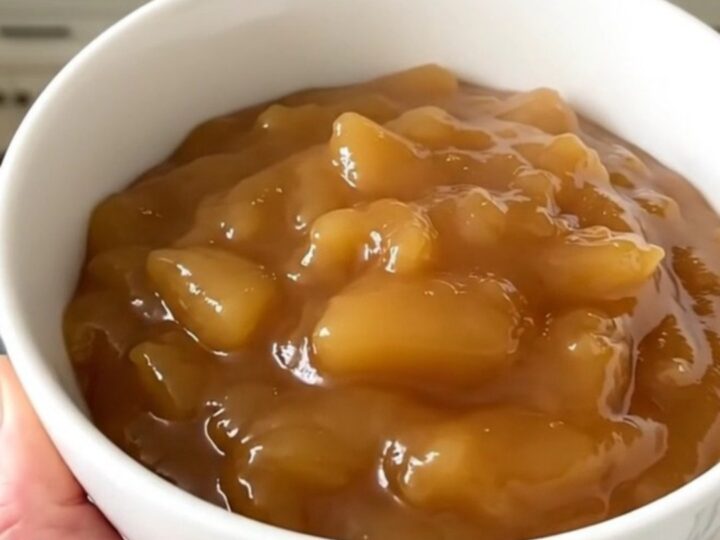 A white bowl filled with glossy, warm, and freshly made cinnamon applesauce.