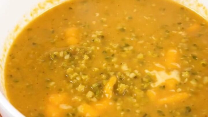 A white bowl of steaming broccoli cheddar soup placed on a table.