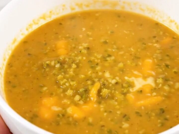 A white bowl of steaming broccoli cheddar soup placed on a table.