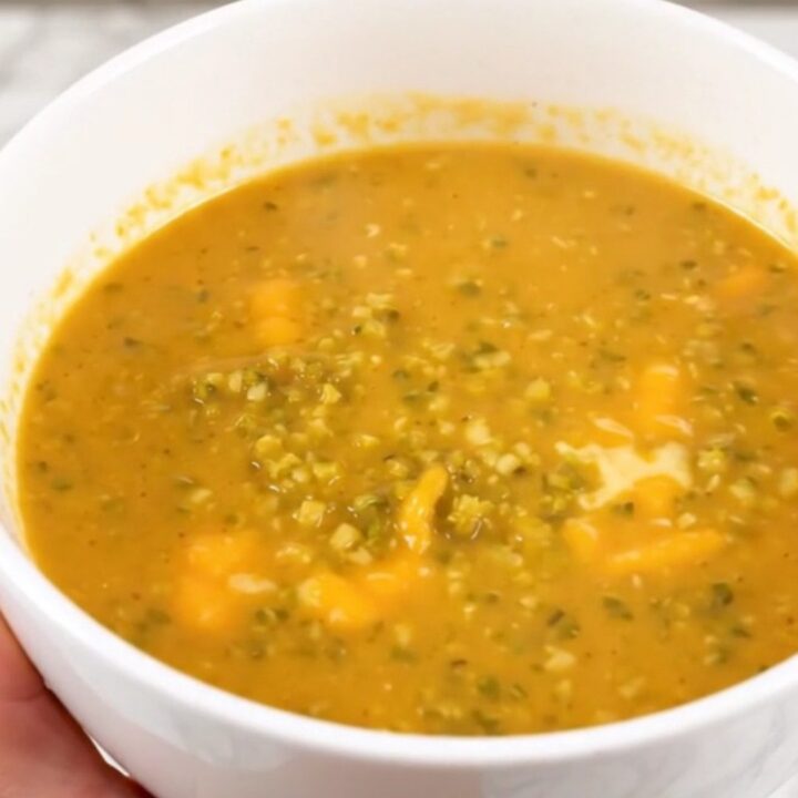 A white bowl of steaming broccoli cheddar soup placed on a table.