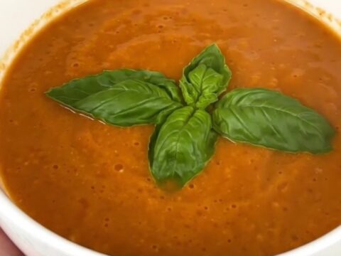 A bowl of creamy tomato basil soup garnished with fresh basil leaves on a bright kitchen counter.