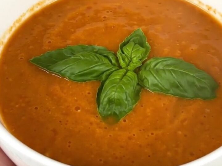 A bowl of creamy tomato basil soup garnished with fresh basil leaves on a bright kitchen counter.