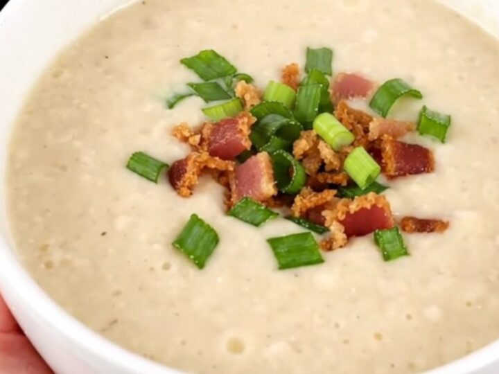 A bowl of creamy, steaming potato bacon leek soup garnished with fresh green scallions.