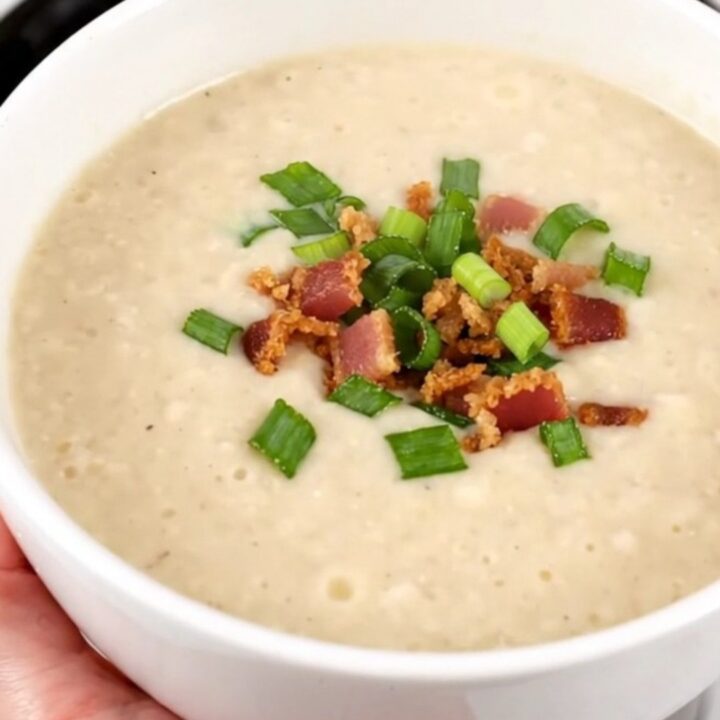 A bowl of creamy, steaming potato bacon leek soup garnished with fresh green scallions.