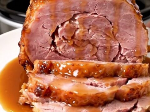 A glossy, spiral-cut bone-in ham with a rich maple Dijon glaze sitting in a slow cooker.