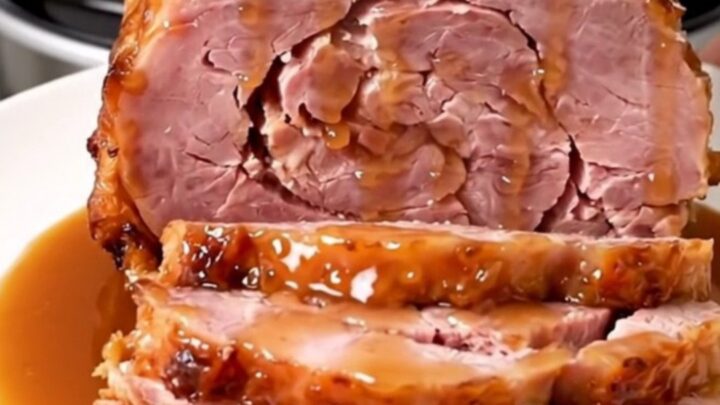 A glossy, spiral-cut bone-in ham with a rich maple Dijon glaze sitting in a slow cooker.