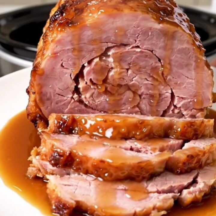 A glossy, spiral-cut bone-in ham with a rich maple Dijon glaze sitting in a slow cooker.