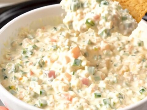 A top-down view of a slow cooker filled with chicken breasts, tomatoes, and a block of cream cheese before cooking.