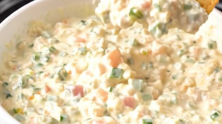 A top-down view of a slow cooker filled with chicken breasts, tomatoes, and a block of cream cheese before cooking.