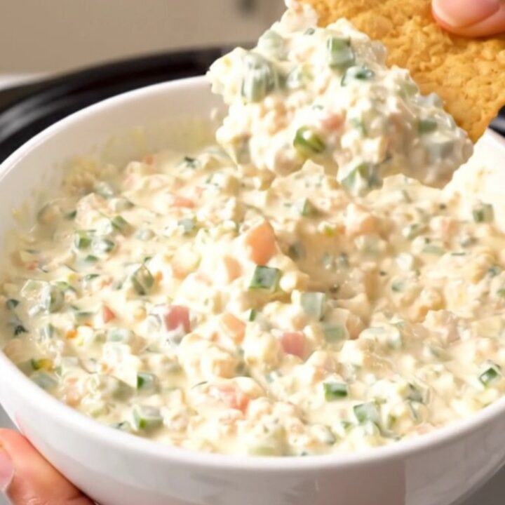 A top-down view of a slow cooker filled with chicken breasts, tomatoes, and a block of cream cheese before cooking.