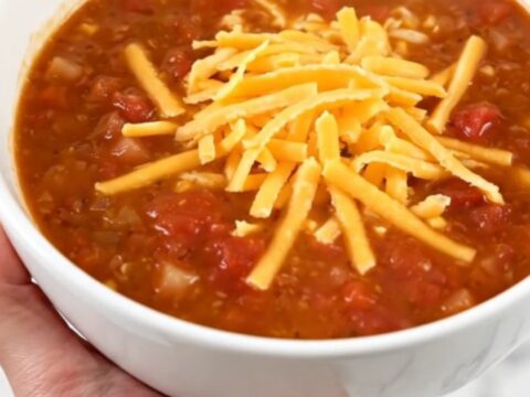 A steaming bowl of taco soup topped with shredded cheddar cheese held in a hand.
