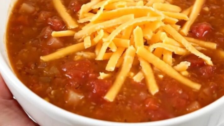 A steaming bowl of taco soup topped with shredded cheddar cheese held in a hand.