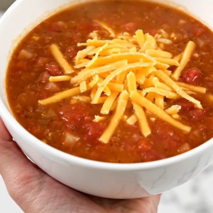 A steaming bowl of taco soup topped with shredded cheddar cheese held in a hand.