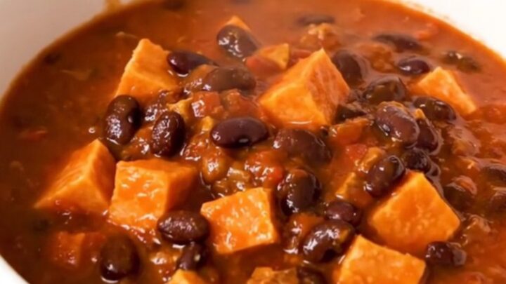 A rustic bowl of slow-cooked sweet potato and black bean chili topped with fresh herbs.
