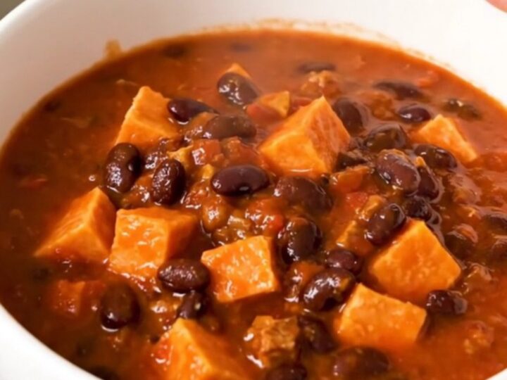 A rustic bowl of slow-cooked sweet potato and black bean chili topped with fresh herbs.
