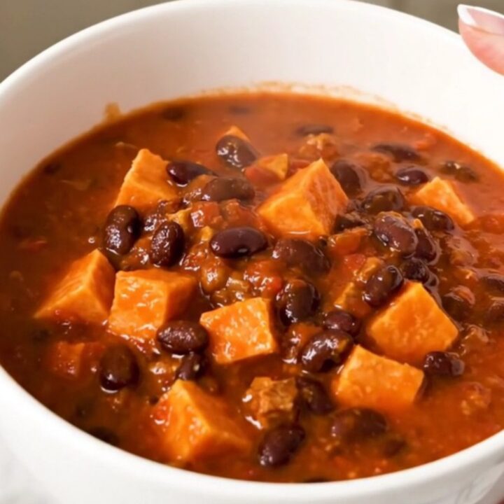 A rustic bowl of slow-cooked sweet potato and black bean chili topped with fresh herbs.