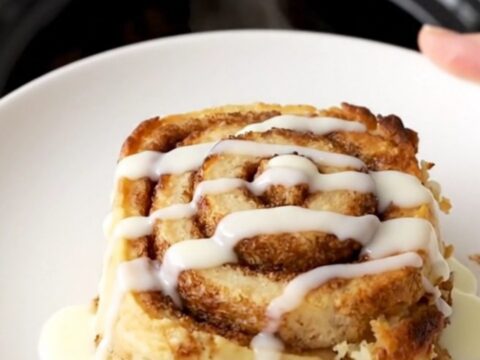 A warm, golden brown cinnamon roll casserole in a slow cooker, topped with a glossy white icing drizzle.