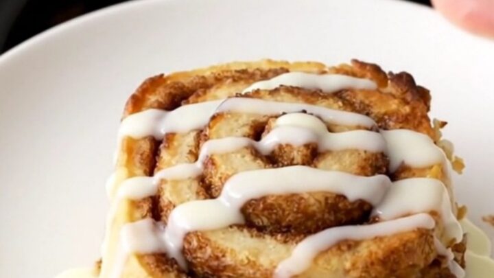 A warm, golden brown cinnamon roll casserole in a slow cooker, topped with a glossy white icing drizzle.