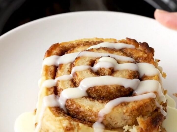 A warm, golden brown cinnamon roll casserole in a slow cooker, topped with a glossy white icing drizzle.