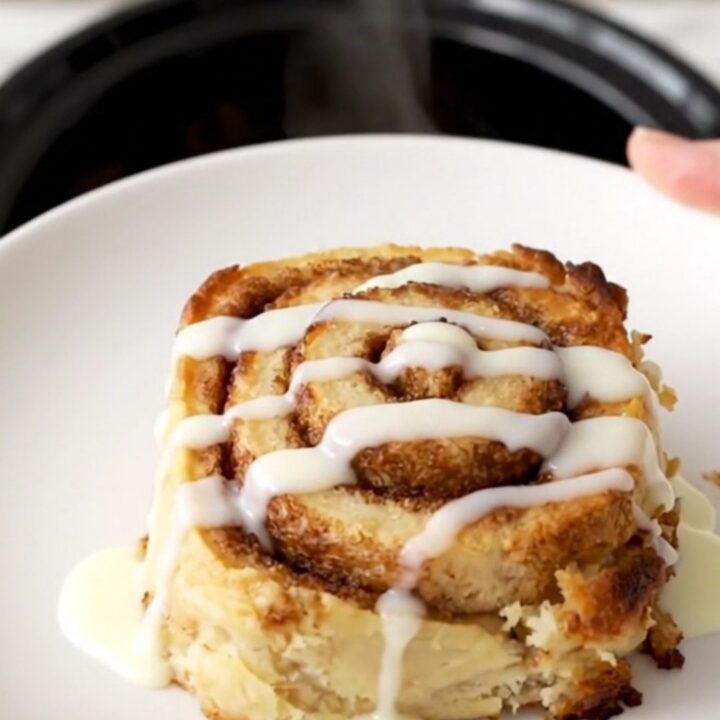 A warm, golden brown cinnamon roll casserole in a slow cooker, topped with a glossy white icing drizzle.