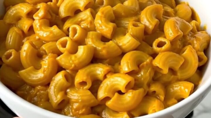 A white bowl filled with creamy pumpkin macaroni and cheese, showing a rich, glossy sauce and tender pasta.