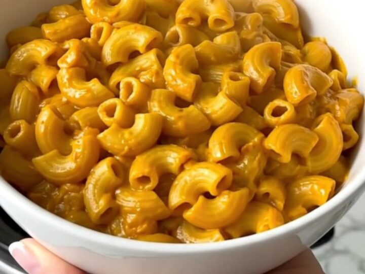 A white bowl filled with creamy pumpkin macaroni and cheese, showing a rich, glossy sauce and tender pasta.