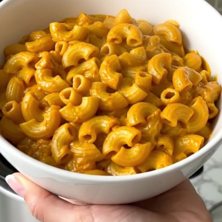 A white bowl filled with creamy pumpkin macaroni and cheese, showing a rich, glossy sauce and tender pasta.