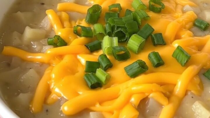 A close-up of a bowl of creamy loaded baked potato soup topped with cheddar cheese and green onions.