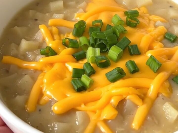 A close-up of a bowl of creamy loaded baked potato soup topped with cheddar cheese and green onions.