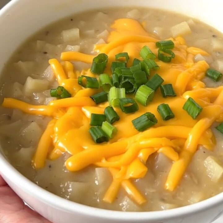 A close-up of a bowl of creamy loaded baked potato soup topped with cheddar cheese and green onions.
