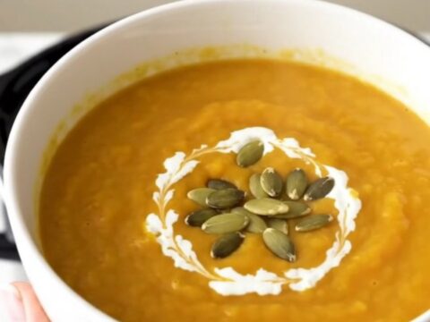 A steaming white bowl of creamy orange butternut squash soup garnished with pumpkin seeds.