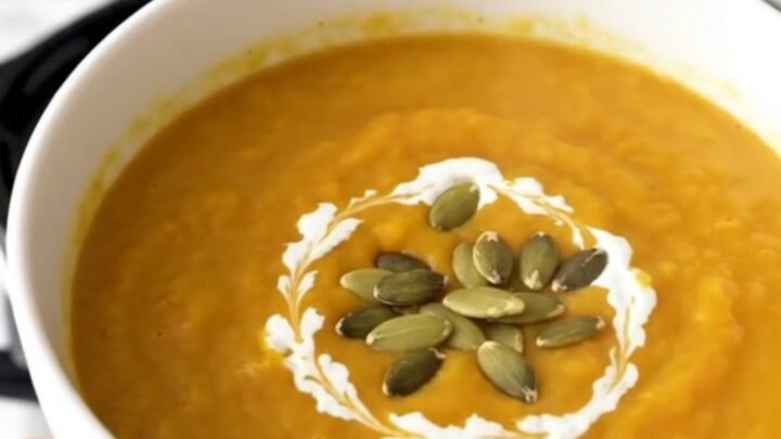 A steaming white bowl of creamy orange butternut squash soup garnished with pumpkin seeds.