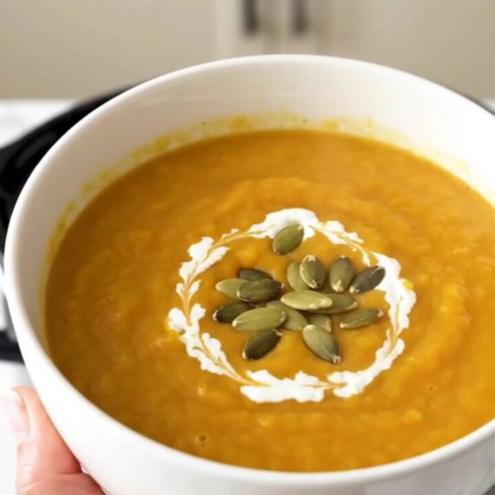 A steaming white bowl of creamy orange butternut squash soup garnished with pumpkin seeds.