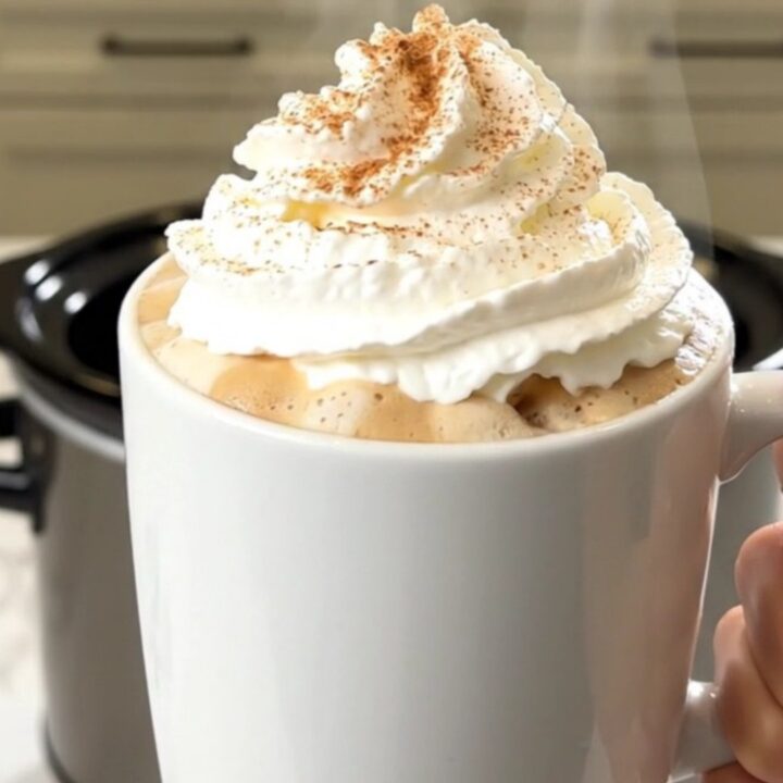 A steaming mug of pumpkin spice latte topped with whipped cream, set against a blurred kitchen background.