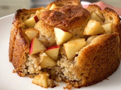 A warm, golden serving of apple cinnamon bread pudding on a white plate.