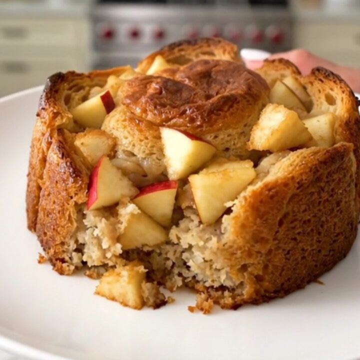 A warm, golden serving of apple cinnamon bread pudding on a white plate.