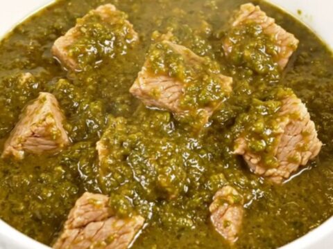 A white bowl filled with steaming, tender green chile pork stew