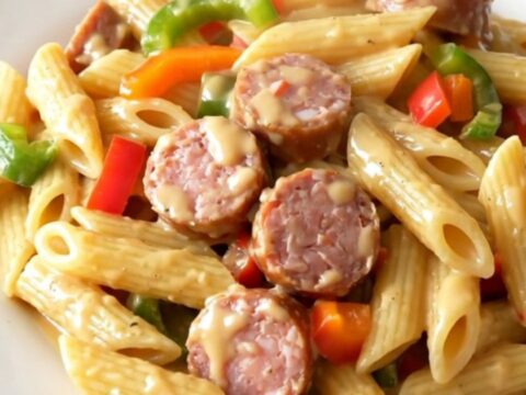 A top-down view of a black slow cooker filled with creamy Cajun sausage pasta on a white quartz countertop.