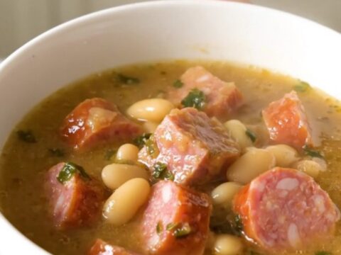 A top-down view of a slow cooker filled with sliced kielbasa, white beans, and seasoned broth before cooking.