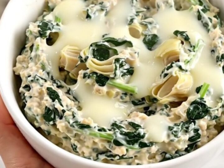 A top-down view into a black slow cooker filled with layers of spinach, artichoke hearts, mozzarella, and cream cheese.