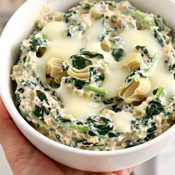 A top-down view into a black slow cooker filled with layers of spinach, artichoke hearts, mozzarella, and cream cheese.