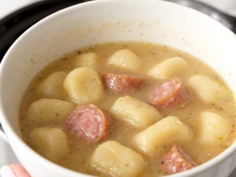 A steaming bowl of creamy sausage and gnocchi soup with fresh spinach in a white bowl.