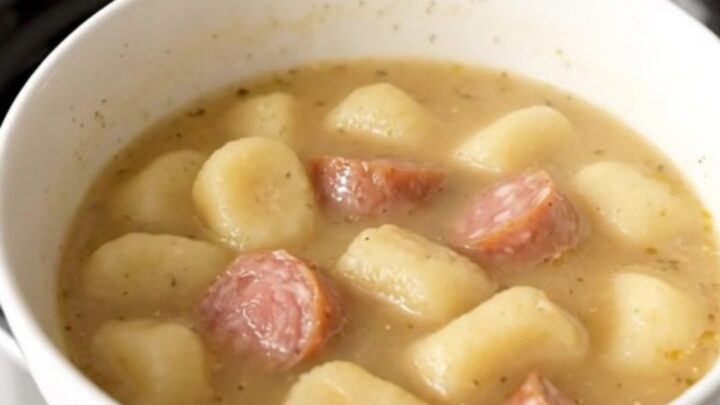 A steaming bowl of creamy sausage and gnocchi soup with fresh spinach in a white bowl.