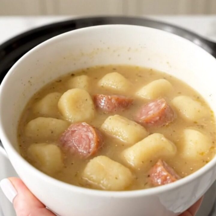 A steaming bowl of creamy sausage and gnocchi soup with fresh spinach in a white bowl.