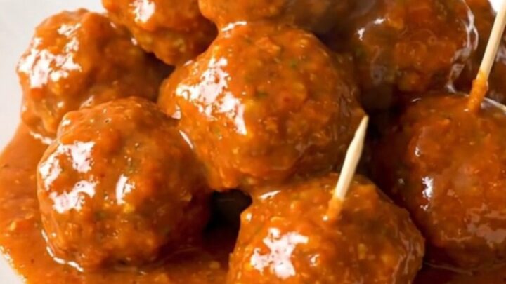 A close-up of glossy buffalo chicken meatballs on a white plate with toothpicks inserted.