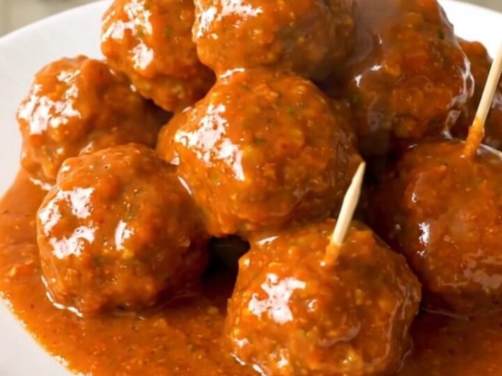 A close-up of glossy buffalo chicken meatballs on a white plate with toothpicks inserted.