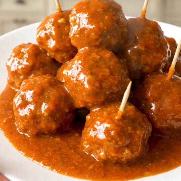 A close-up of glossy buffalo chicken meatballs on a white plate with toothpicks inserted.