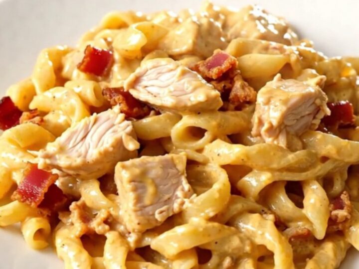 A top-down view of chicken, bacon, and alfredo sauce in a slow cooker.