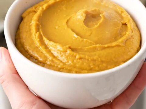 A warm, smooth pumpkin cheesecake dip in a white bowl with crackers ready for serving.